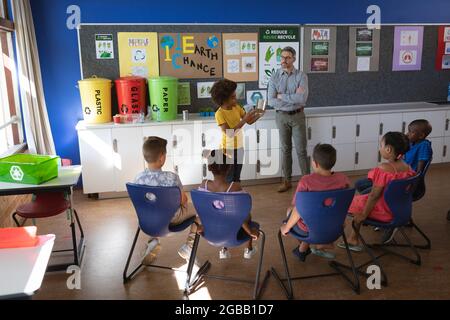 African american boy showing how to recycle plastic items to other students in class at school Stock Photo