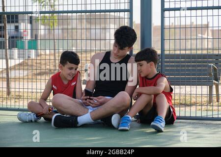 Elder brother showing something on the smartphone to his younger siblings. One of the kids has a leg prosthesis. Stock Photo
