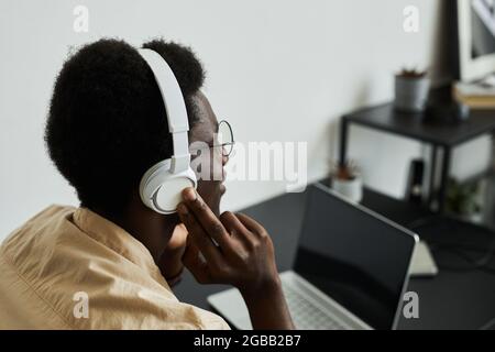 Rear view of African businessman putting on wireless headphones while talking online on laptop at the table Stock Photo