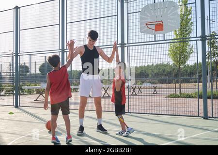 Basketball players high fiving with their coach, one of them has a leg prosthesis. Coach motivating kids during time out. Stock Photo