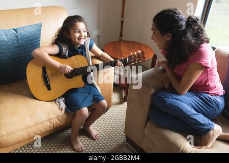 Mixed race mother and daughter sitting on sofa and playing guitar Stock Photo