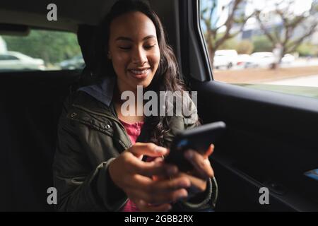 Smiling asian woman sitting in taxi, using smartphone Stock Photo