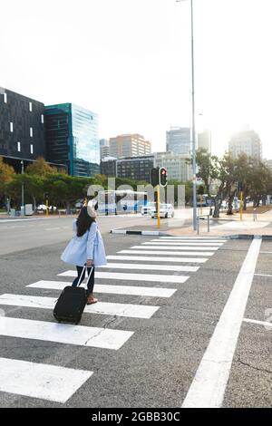 Asian woman crossing road with suitcase Stock Photo