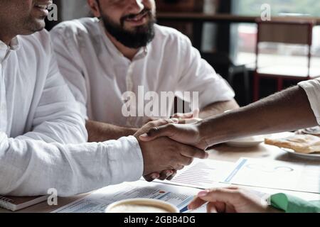 Two Muslim businessmen shaking hands over financial papers on workplace Stock Photo