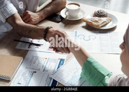 Young Arabic businesswoman shaking hand of male business partner over table Stock Photo