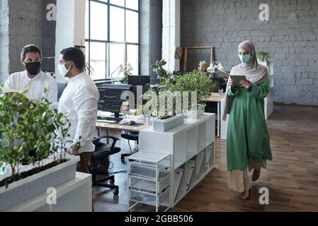 Young Muslim female with tablet walking along open space office Stock Photo