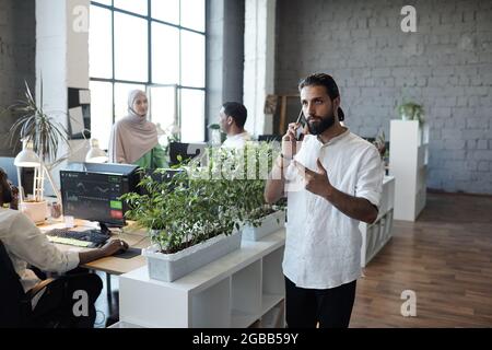 Young serious Muslim businessman consulting client on mobile phone in working environment Stock Photo