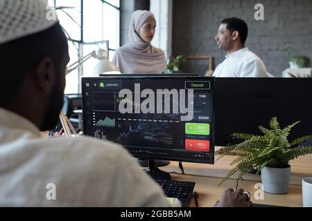 Two intercultural Muslim office managers discussing working points in front of computer monitors Stock Photo