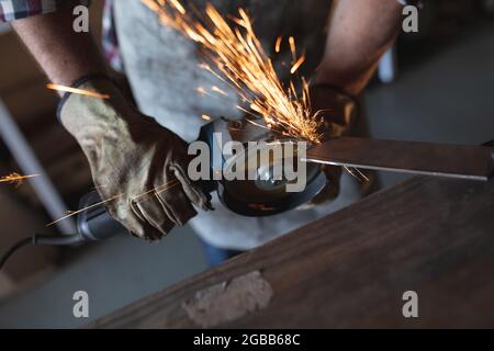 Hands of caucasian male knife maker wearing apron, using angle grinder in workshop Stock Photo
