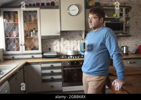 Focused caucasian man wearing glasses, standing in kitchen drinking coffee Stock Photo