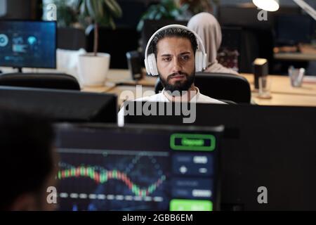 Bearded Arabic businessman in headphones looking at computer screen in office environment Stock Photo