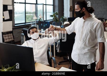Young successful businessmen with protective masks bumping elbows instead of handshake