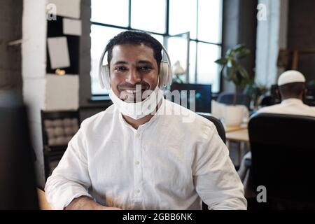Young successful mixed-race businessman in headphones looking at you with toothy smile Stock Photo
