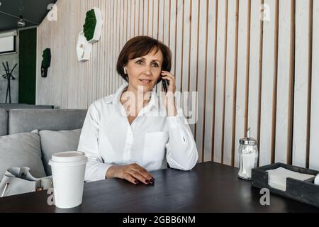 Senior businesswoman in white blazer work in cafe. Remote work. Stock Photo