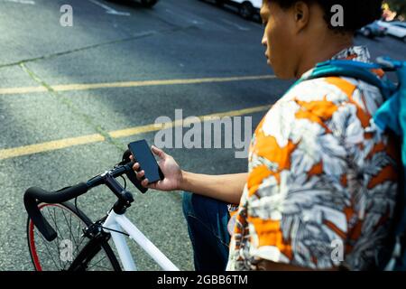 African american man in city sitting on bike and using smartphone Stock Photo