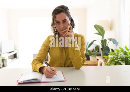Portrait of caucasian woman having a video call, taking notes and smiling Stock Photo