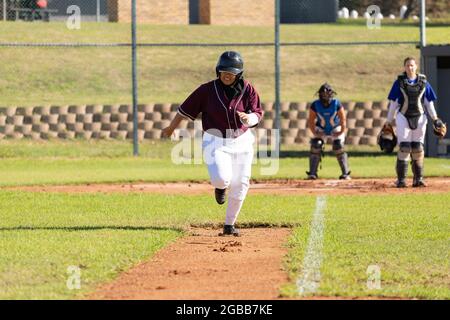 Mixed race female baseball player on sunny baseball field running between bases during game Stock Photo