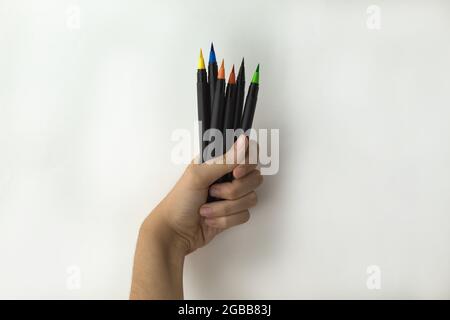 hand of a girl holding a handful of color pens and markers on white background Stock Photo