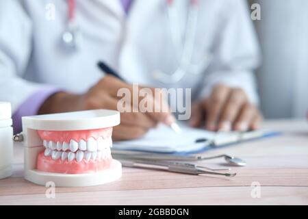 doctor hand writing prescription with plastic dental teeth model on table  Stock Photo