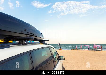 Side view of big family white suv van car with big rooftop cargo rack box at scenic sand seaside campsite camp coast of sea or ocean sky on background Stock Photo