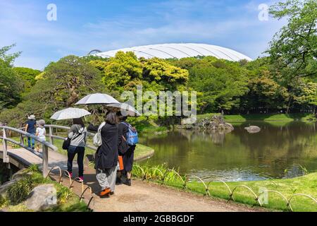 tokyo, japan - may 03 2021: Japanese tourists holding sun umbrellas and walking on the bridge of Koishikawa Korakuen Park along the lake with the Hora Stock Photo