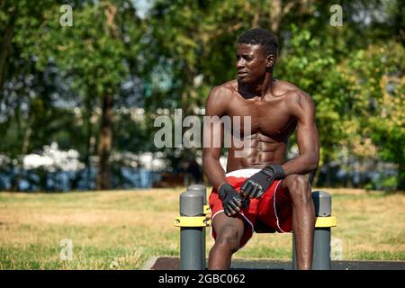 Athlete doing push-ups on the sports ground, African American athlete doing push-ups on outdoor gym equipment, sports lifestyle, striving for success. Stock Photo