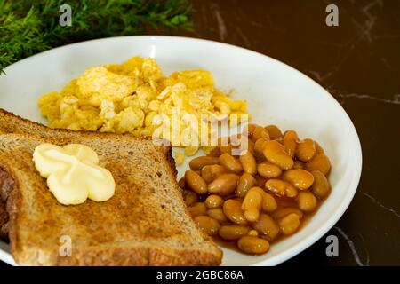 Close-up of a healthy breakfast with toasted bread, butter, baked beans and scramble eggs. Selective focus points Stock Photo