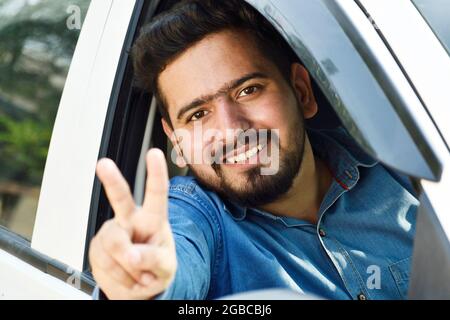 car loan concept, happy indian man showing victory sign from car window Stock Photo