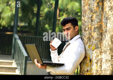 Young Indian Businessman Working Outdoor On Laptop and Drinking Coffee Stock Photo