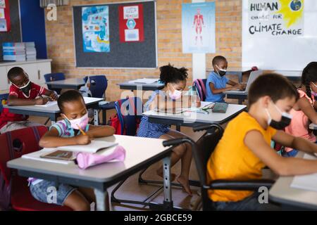 Group of students wearing face masks studying while sitting on their desks at elementary school Stock Photo