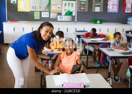 Portrait of african american female teacher and disabled girl smiling in class at elementary school Stock Photo