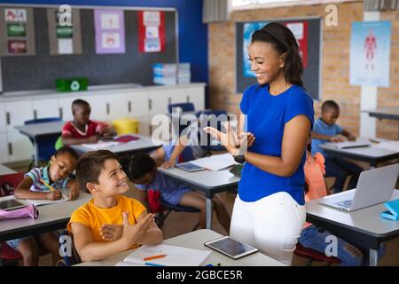 African american female teacher and caucasian boy talking in hand sign language at elementary school Stock Photo