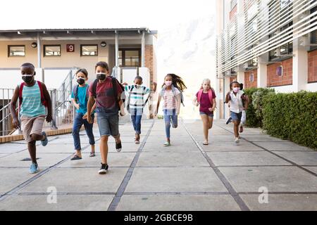 Group of diverse students wearing face masks running at elementary school Stock Photo