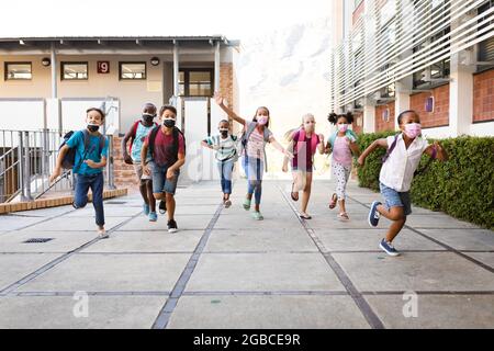 Group of diverse students wearing face masks running at elementary school Stock Photo
