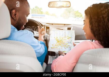Happy black couple looking at paper map sitting inside car Stock Photo