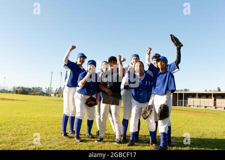 Portrait of diverse group of female baseball players and coach standing and cheering on sunny field Stock Photo