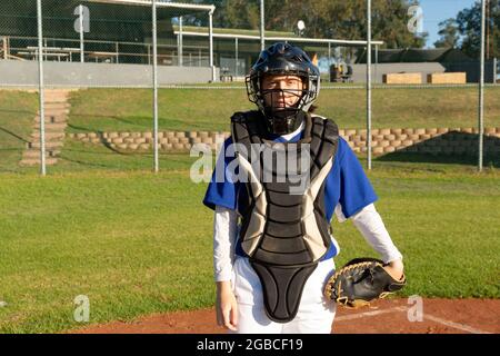 Portrait of caucasian female baseball player standing on field in catcher's body shield and helmet Stock Photo