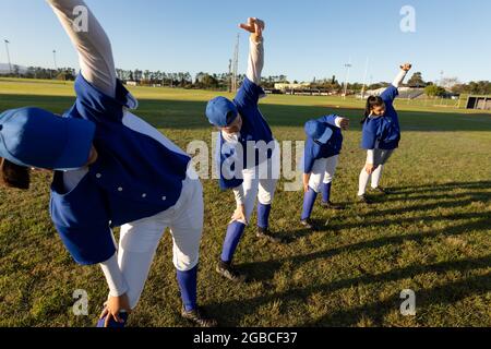 Diverse group of female baseball players warming up on field, stretching from the waist Stock Photo