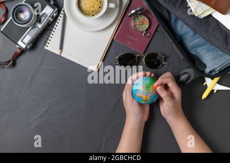 Pin on the world map and Prepare a suitcase,  vintage camera,  notebook, passport, map and hot coffee on black background. travel concept Stock Photo