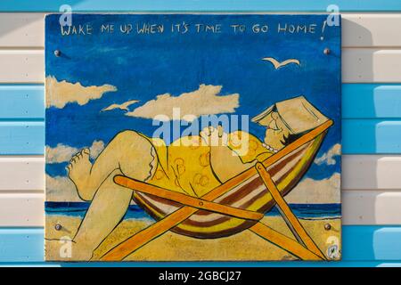 England, Hampshire, Hayling Island, Funny Painting of Fat Lady Asleep in Deck Chair on side of Colourful Beach Hut Stock Photo