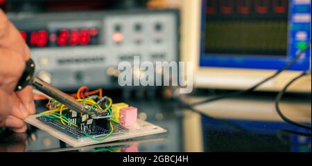 Manufacturing and setting up an electronic device in the laboratory. Soldering iron and electronic measuring instruments Stock Photo