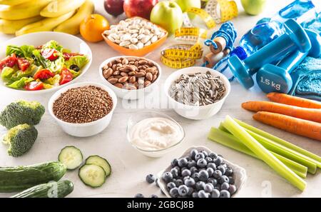 Selection of healthy foods, vegetables, fruits, almonds, salad, exercise tools and measuring tape. Stock Photo
