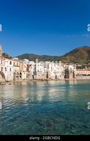 Cefalù, Palermo, Sicily, Italy. View across tranquil harbour to the Old Town, overhanging houses clustered together along waterfront. Stock Photo