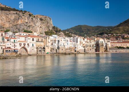 Cefalù, Palermo, Sicily, Italy. View across tranquil harbour to the Old Town, overhanging houses clustered together along waterfront beneath La Rocca. Stock Photo