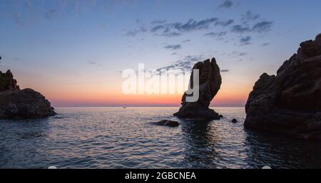 Cefalù, Palermo, Sicily, Italy. Panoramic view across the tranquil waters of Calura Bay, dawn, towering rock stack silhouetted against colourful sky. Stock Photo