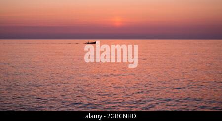 Cefalù, Palermo, Sicily, Italy. Panoramic view across the tranquil waters of Calura Bay, sunrise, lone fisherman heading out to sea. Stock Photo