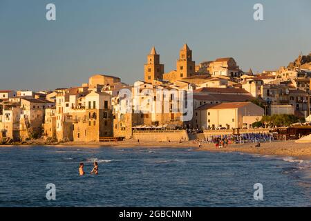 Cefalù, Palermo, Sicily, Italy. View from water's edge along sandy beach to the imposing twin towers of the Arab-Norman cathedral, sunset. Stock Photo