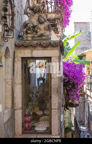 Taormina, Messina, Sicily, Italy. Typical flower-filled alley off Corso Umberto I, antique shop façade draped in pink bougainvillea. Stock Photo