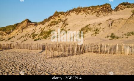 Natural reserve hills sand  dunes at the sea by the sun set behind a protective wooden fence, covered by grass. Clean beach. Sign in French: "Fragile". Stock Photo