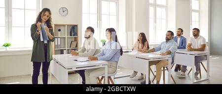 Business coach teaching group of adult students who are sitting at desks in classroom Stock Photo